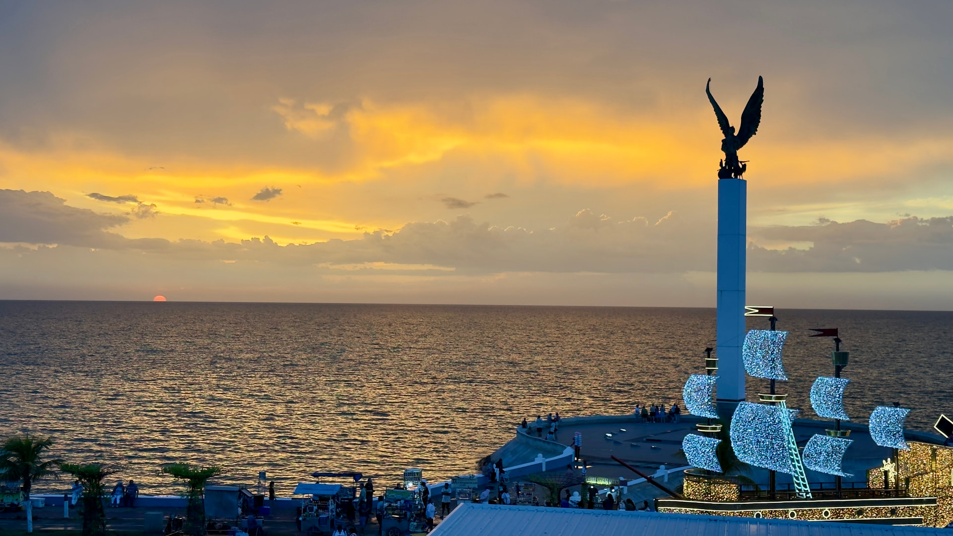 Atardecer dorado sobre el Golfo de México desde el malecón de Campeche con el monumento del Ángel y el barco iluminado